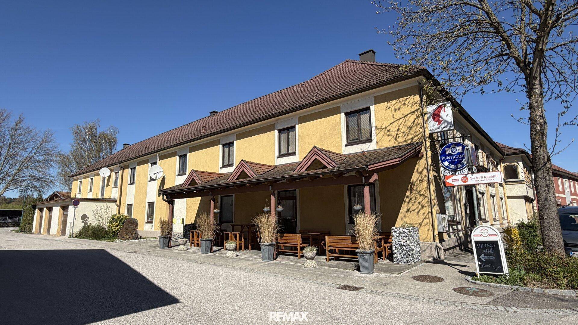 Gasthaus mit überdachtem Außenbereich und traditioneller Architektur unter strahlendem Sonnenschein.