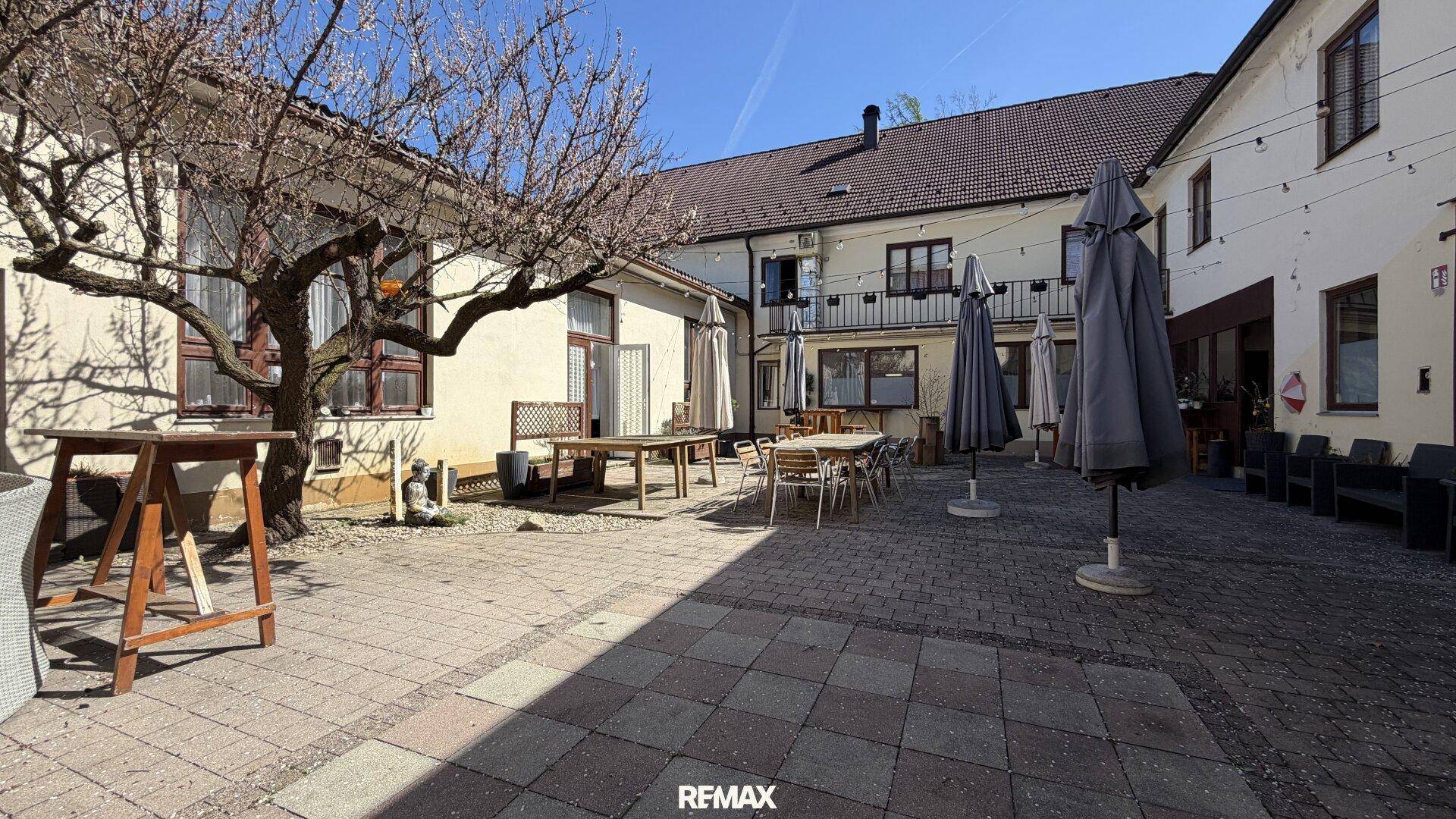 Sonniger Innenhof mit Pflastersteinen, Sitzgelegenheiten und großen Sonnenschirmen.