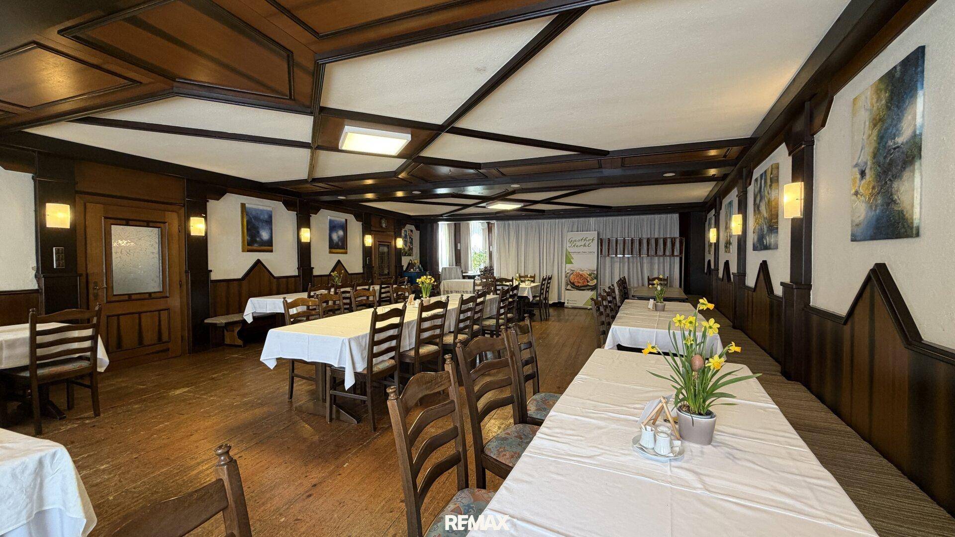 Weiter Blick in den Speisesaal mit langen Tischen, Holzboden und dekorativen Wandbildern.