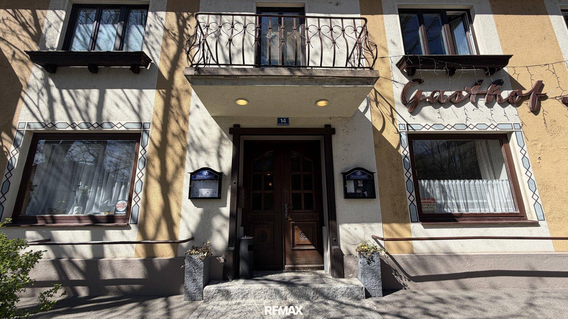 Haupteingang des Gasthofs mit Holztür, französischem Balkon und dekorativen Elementen.