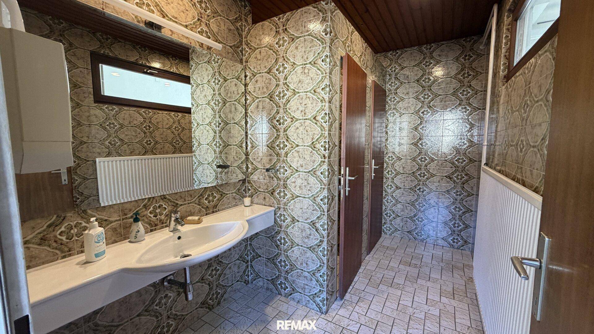 Damen-WC mit gemusterten Fliesen, Einzelwaschbecken und Holzdecke.