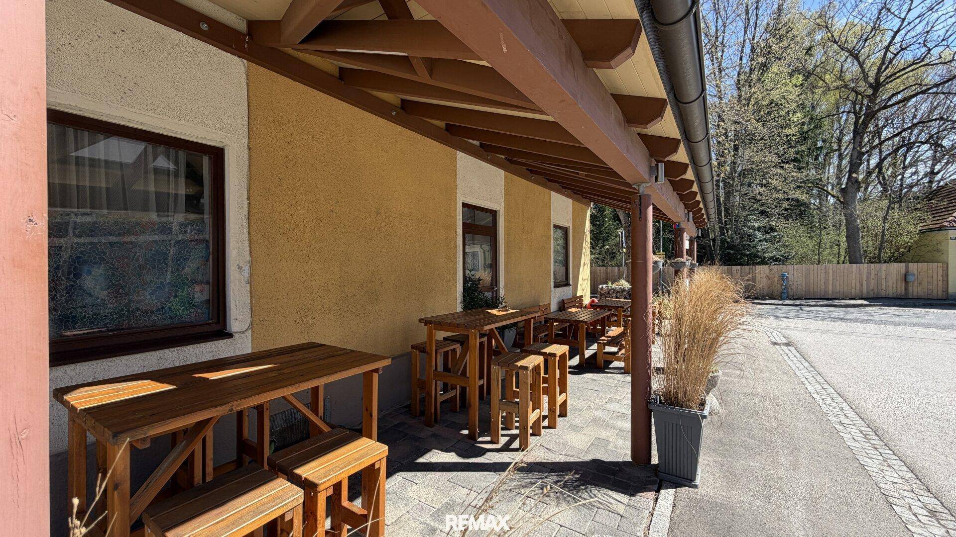 Überdachte Terrasse mit Holztischen und Bänken, ideal für Mahlzeiten im Freien.