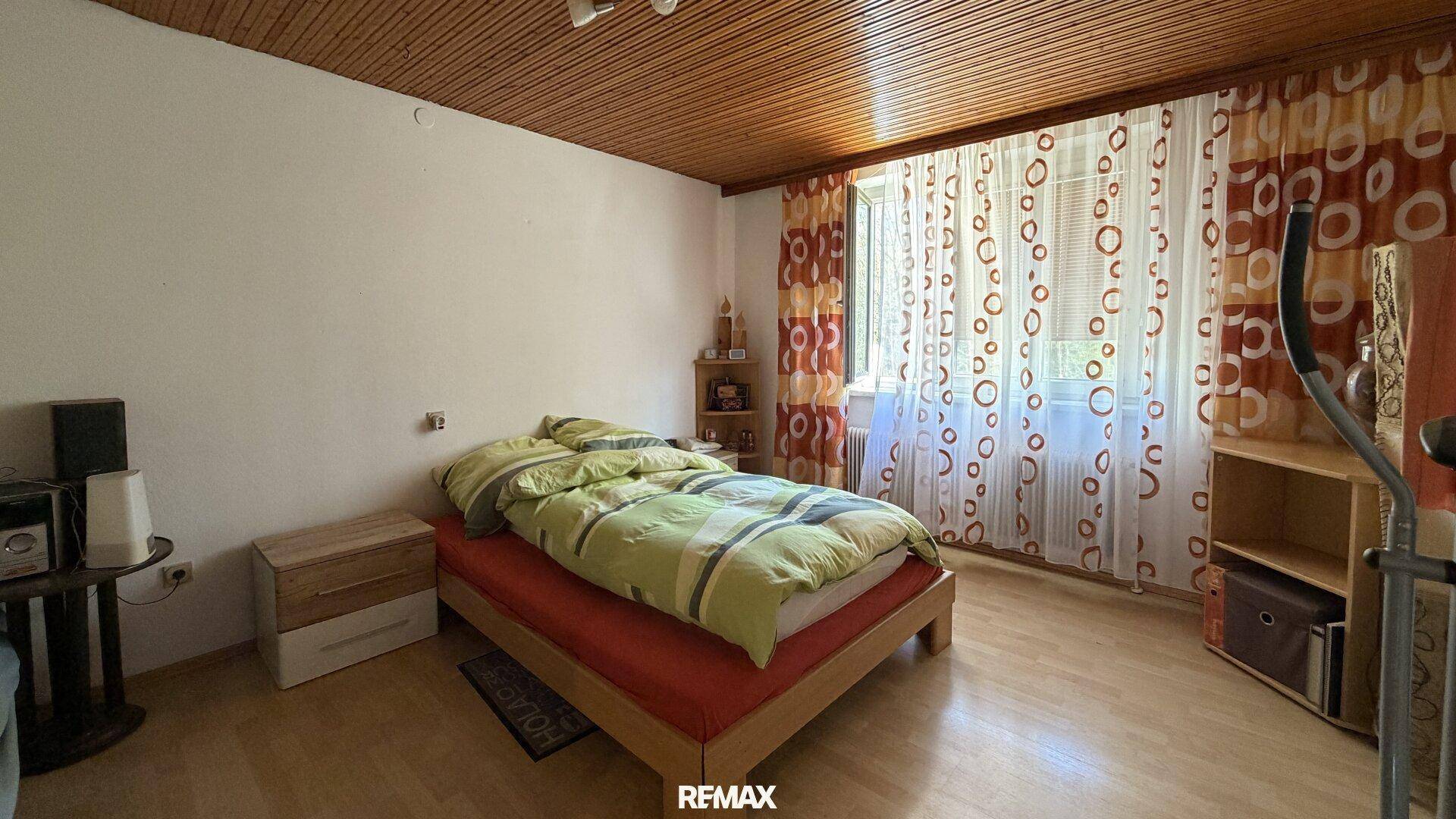 Schlafzimmer mit Einzelbett, Holzdecke und gemusterten Vorhängen, inklusive Trainingsgerät.