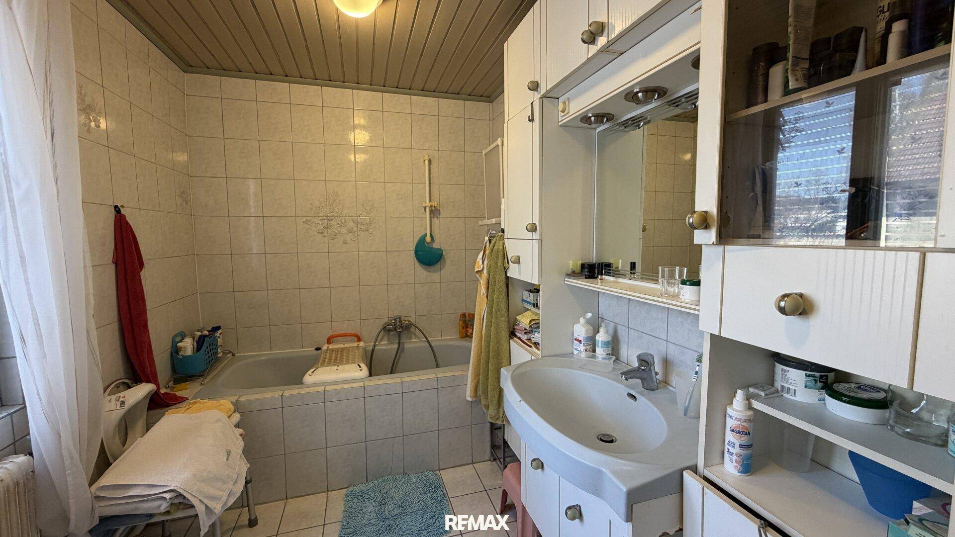 Älteres Badezimmer mit Badewanne, Waschbecken und Spiegelschrank, komplett gefliest.