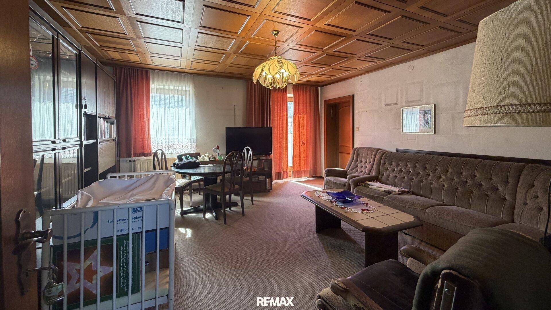 Wohn-Esszimmer mit Kassettendecke aus Holz, Sofa, Esstisch und Babybett, in traditionellem Stil.