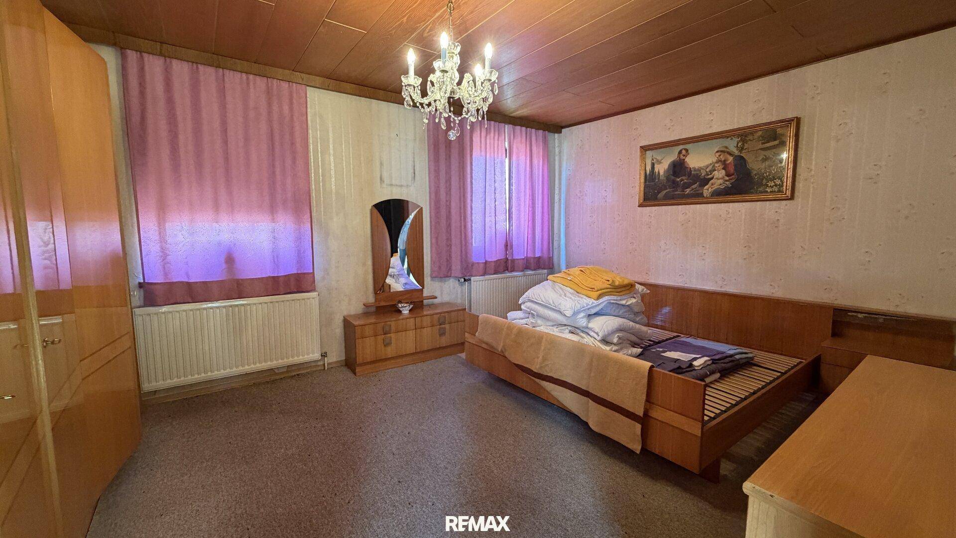 Schlafzimmer mit Holzbett, Holzdecke und lila Vorhängen, in einem traditionellen Ambiente.