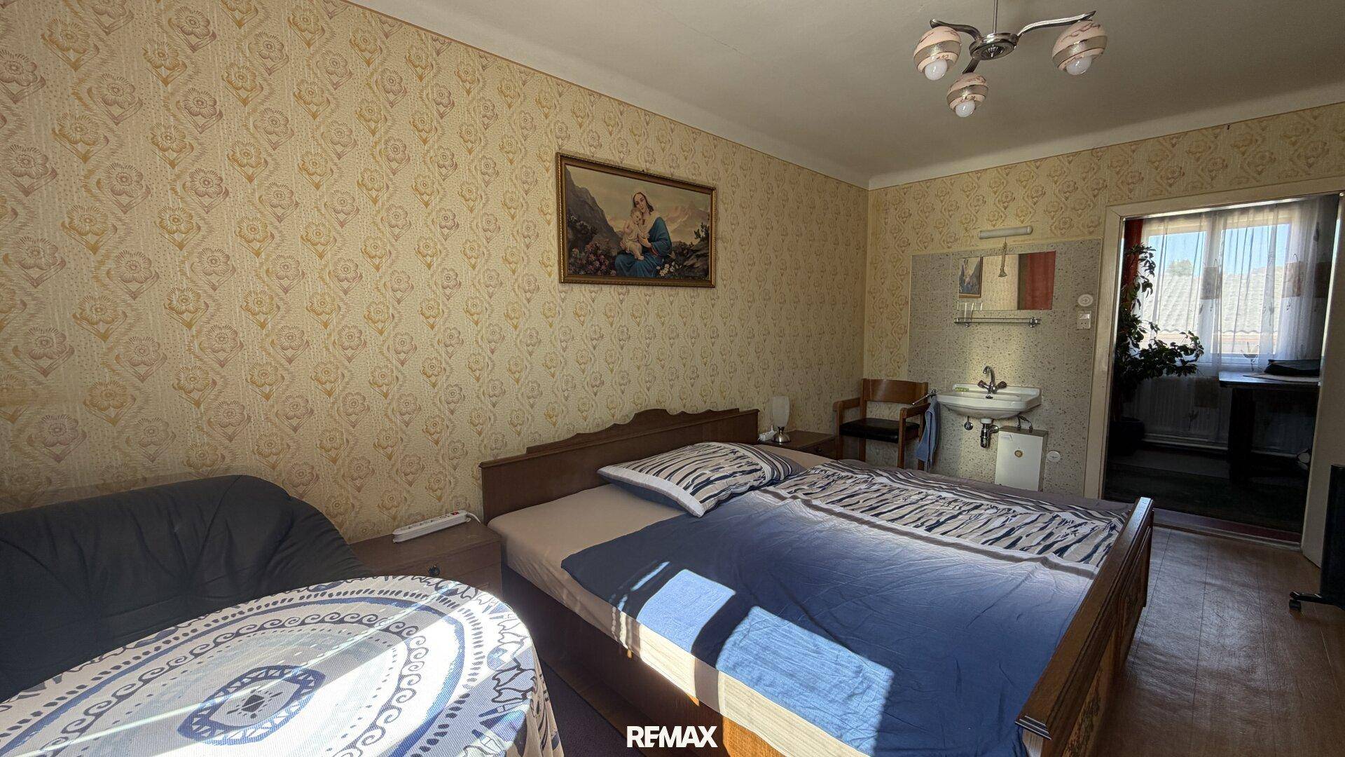 Schlafzimmer mit Bett, Waschbecken und gemusterter Tapete, in einem funktionalen Zustand.