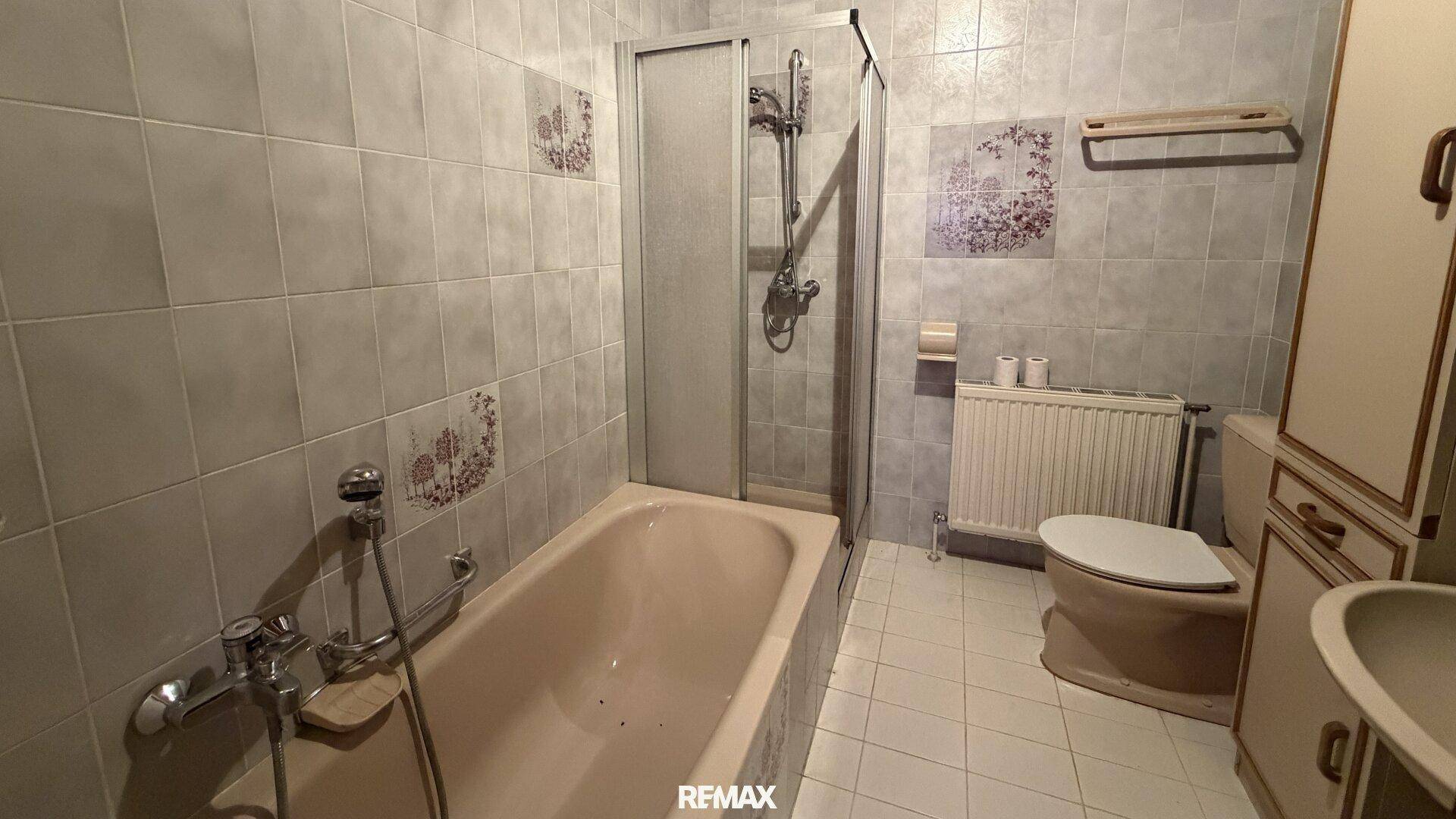 Älteres Badezimmer mit Badewanne, Duschkabine, Toilette und Waschbecken, komplett gefliest.