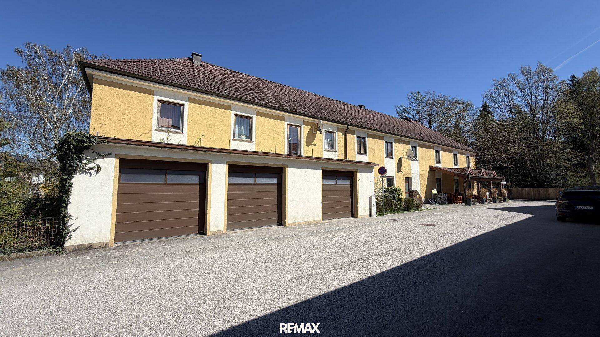 Lange Gebäudefassade mit mehreren Garagentoren und Fenstern, in ländlicher Umgebung.