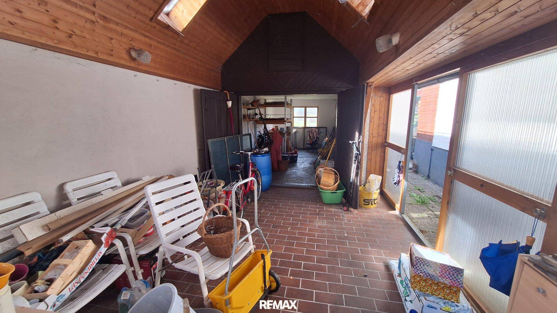 Überdachter Bereich mit Ziegelboden, Stauraum und Zugang zum Garten.
