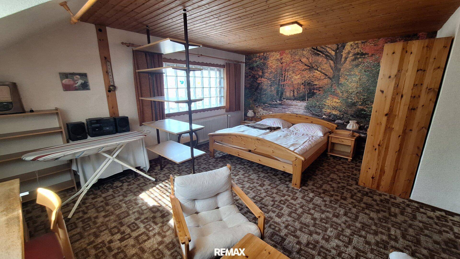 Schlafzimmer im Dachgeschoss mit Holzbett, Teppichboden und dekorativer Wandtapete.