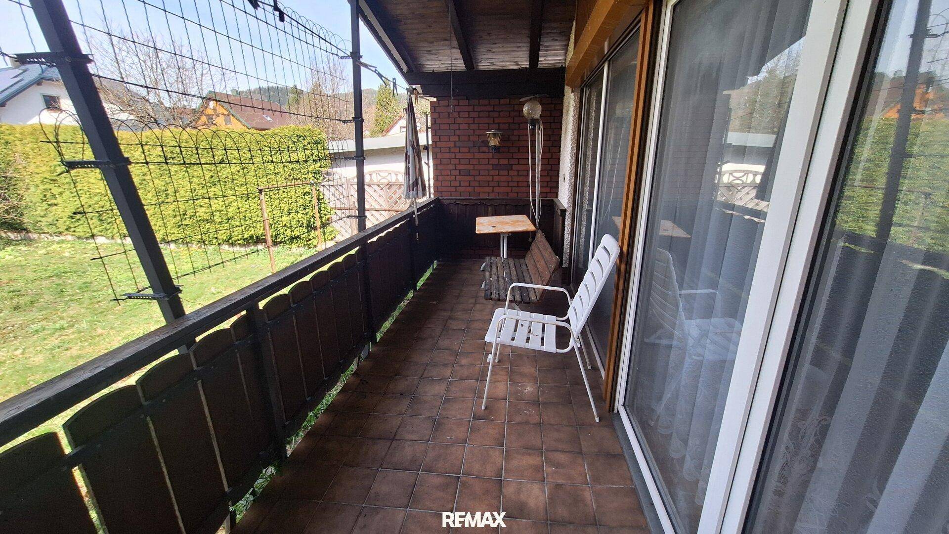 Überdachter Balkon mit Fliesenboden, Sitzgelegenheiten und Blick in den Garten.