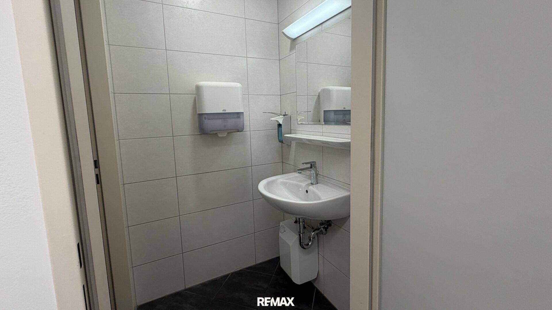 Kleine Toilette mit Waschbecken und Fliesen an Wänden und Boden, sauber und funktional.