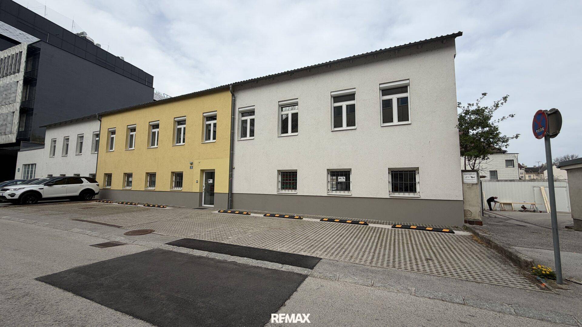 Ansicht eines Geschäftsgebäudes mit gelber und weißer Fassade sowie Parkmöglichkeiten im Vordergrund.