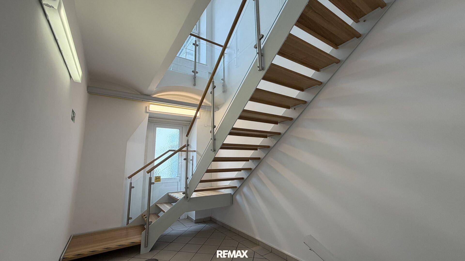 Moderne Treppe mit Holzstufen und Glasgeländer, die viel Licht durch ein Fenster erhält.