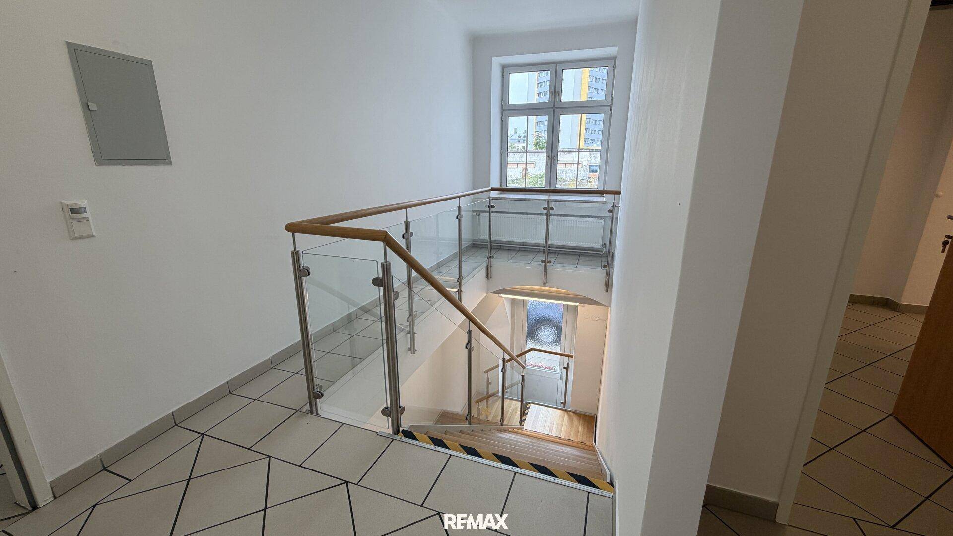 Treppenabsatz mit Glasgeländer und Blick auf ein Fenster, das den Bereich hell erleuchtet.