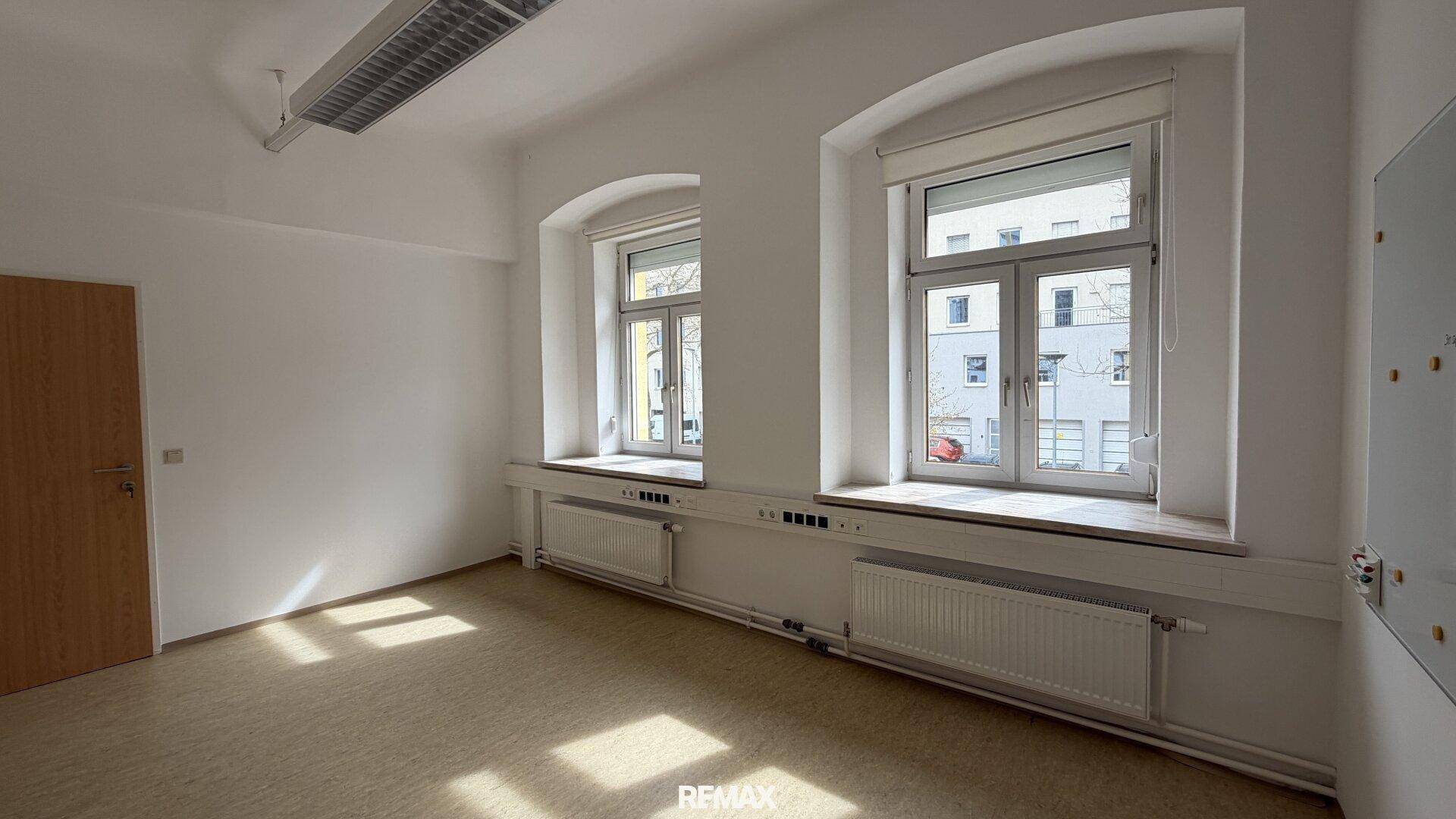 Heller Büroraum mit zwei großen Fenstern und einem strapazierfähigen Bodenbelag, ideal für Arbeitsbereiche.