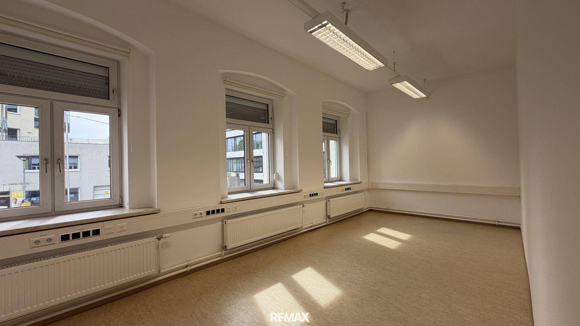 Heller Büroraum mit mehreren Fenstern entlang der Wand, die für eine optimale Belichtung sorgen.