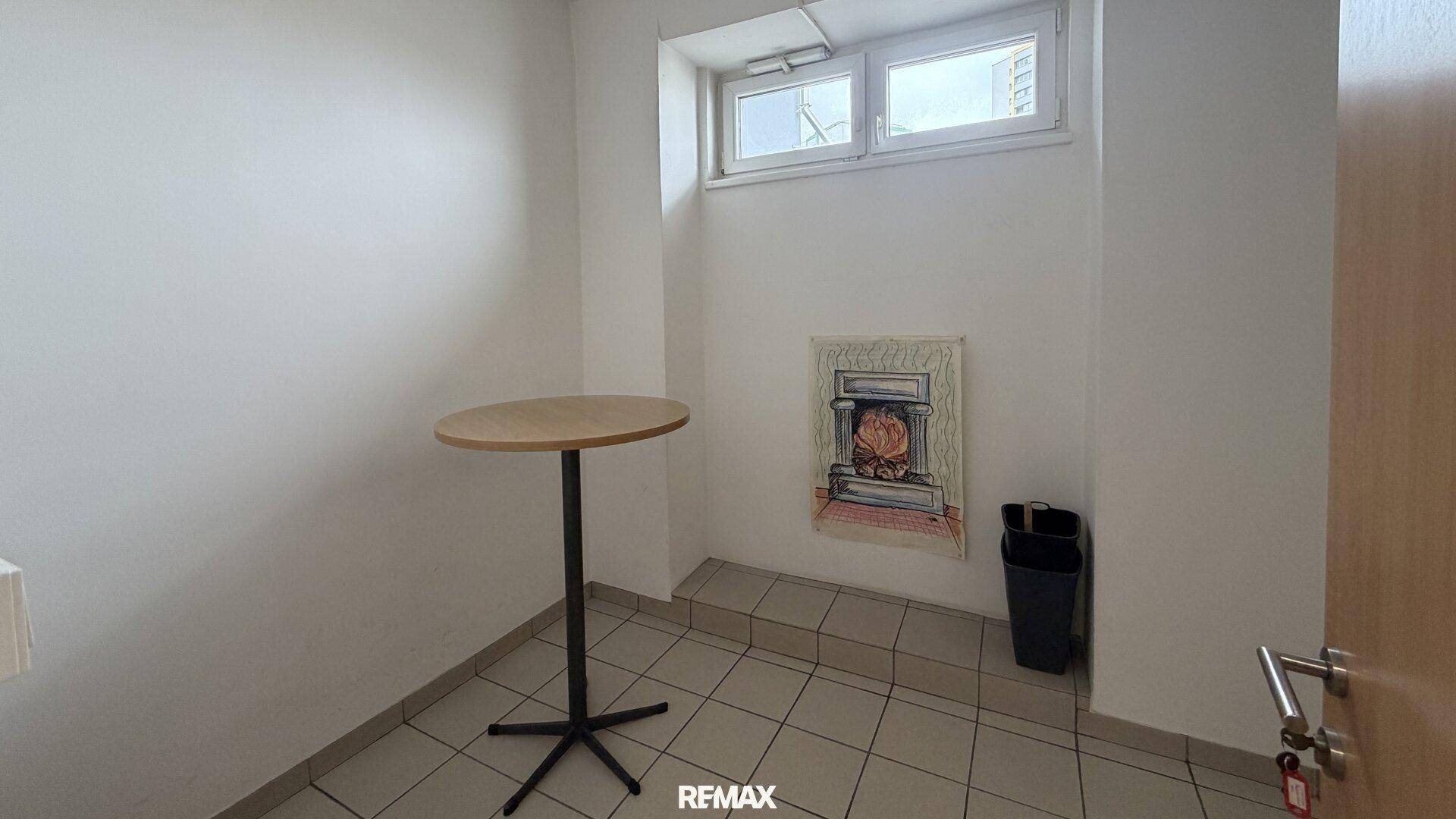 Kleiner Pausenraum mit einem Stehtisch und einem Fenster, ideal für kurze Erholungspausen.