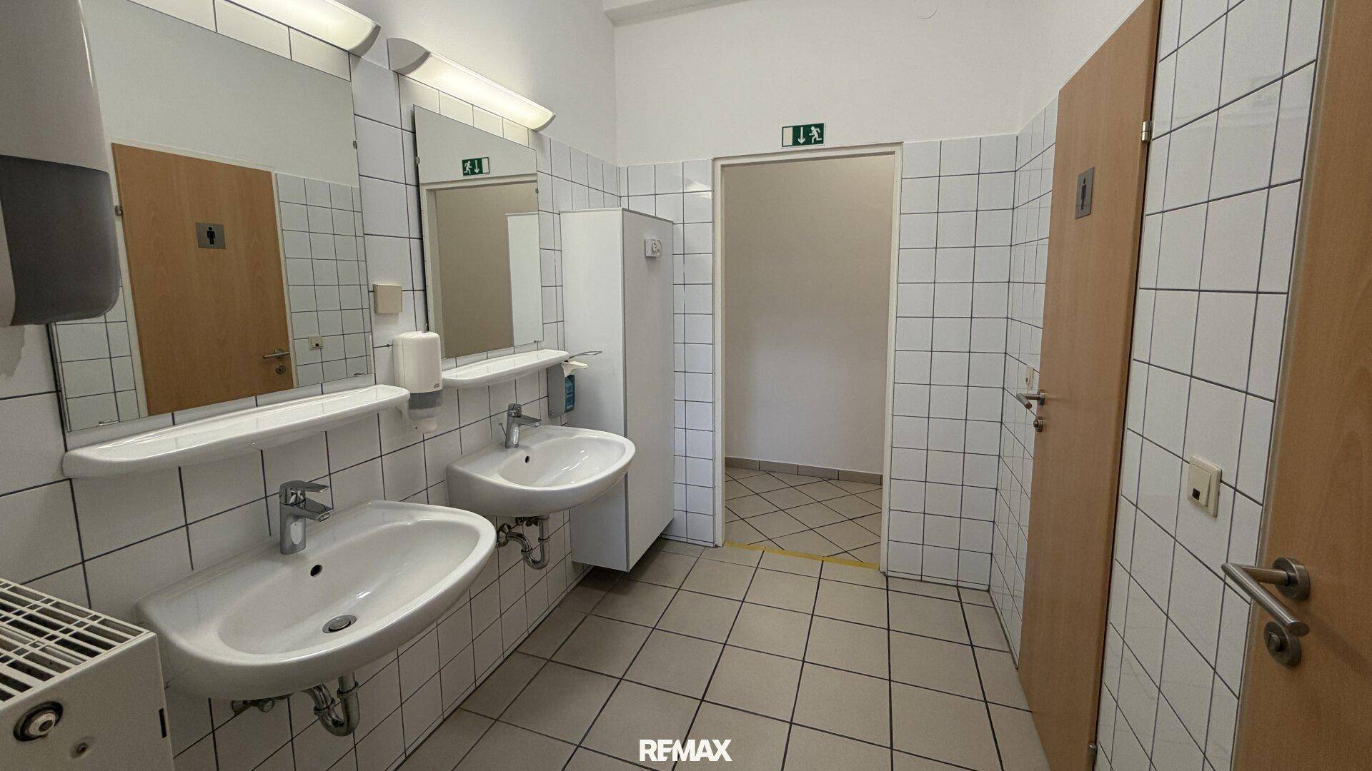 Geräumiger Waschraum mit zwei Waschbecken, großen Spiegeln und gefliesten Wänden.