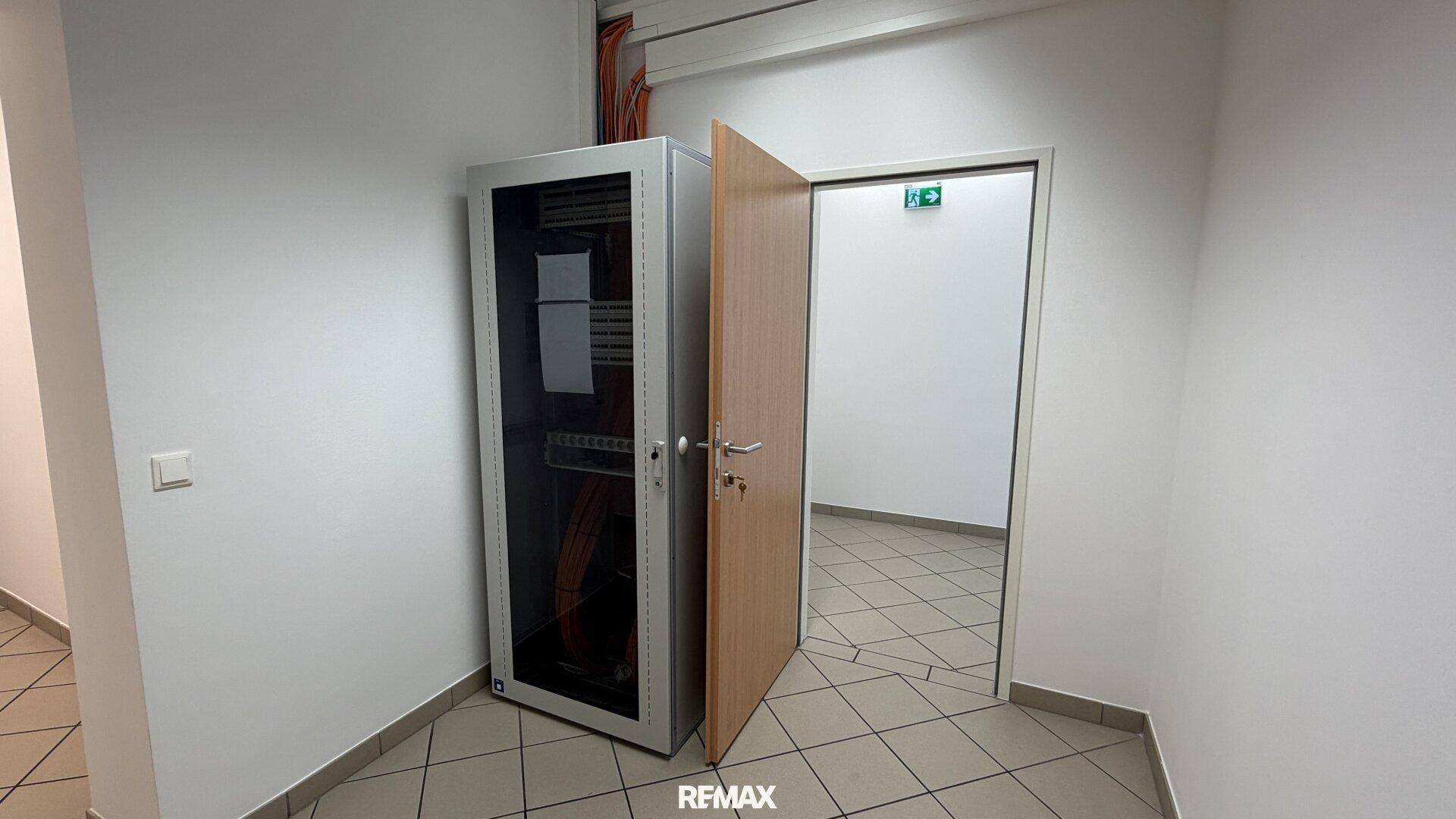 Serverschrank in einem kleinen Raum mit Fliesenboden und Holztür.