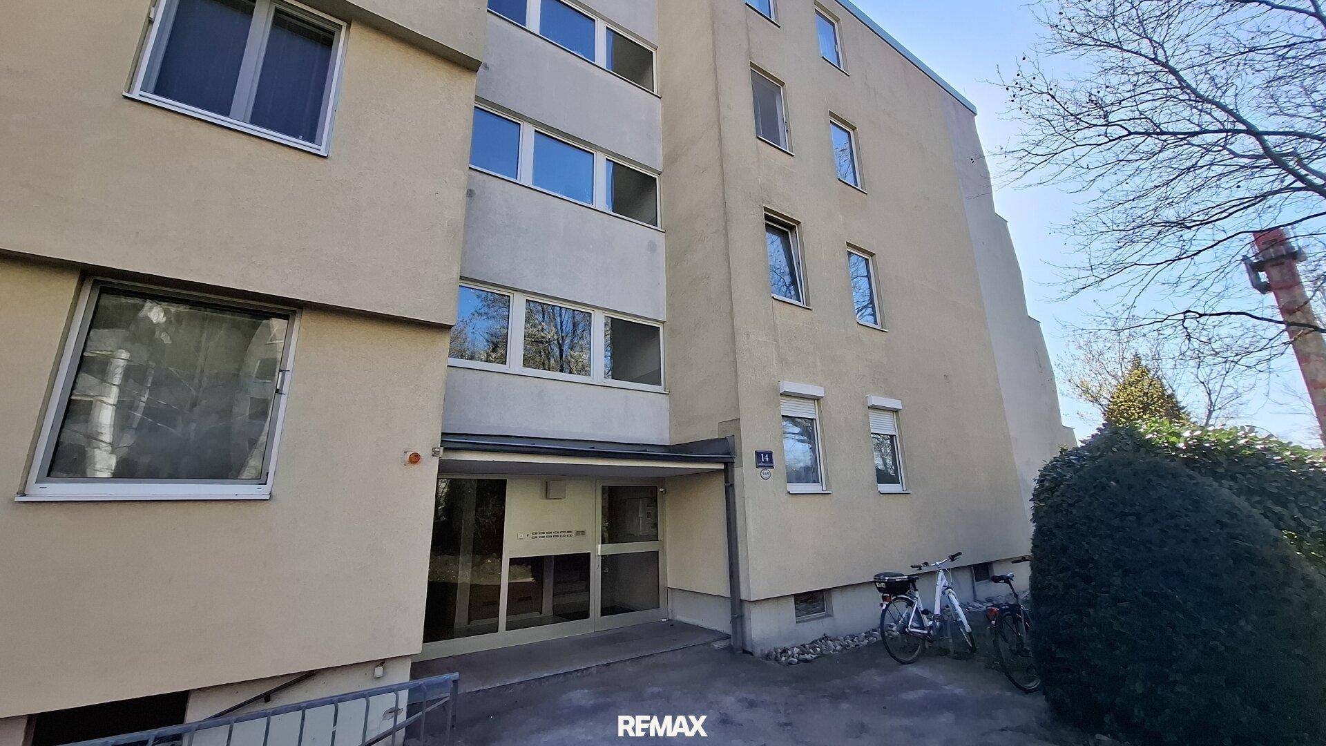 Eingangsbereich eines Mehrfamilienhauses mit beiger Fassade und geparkten Fahrrädern.