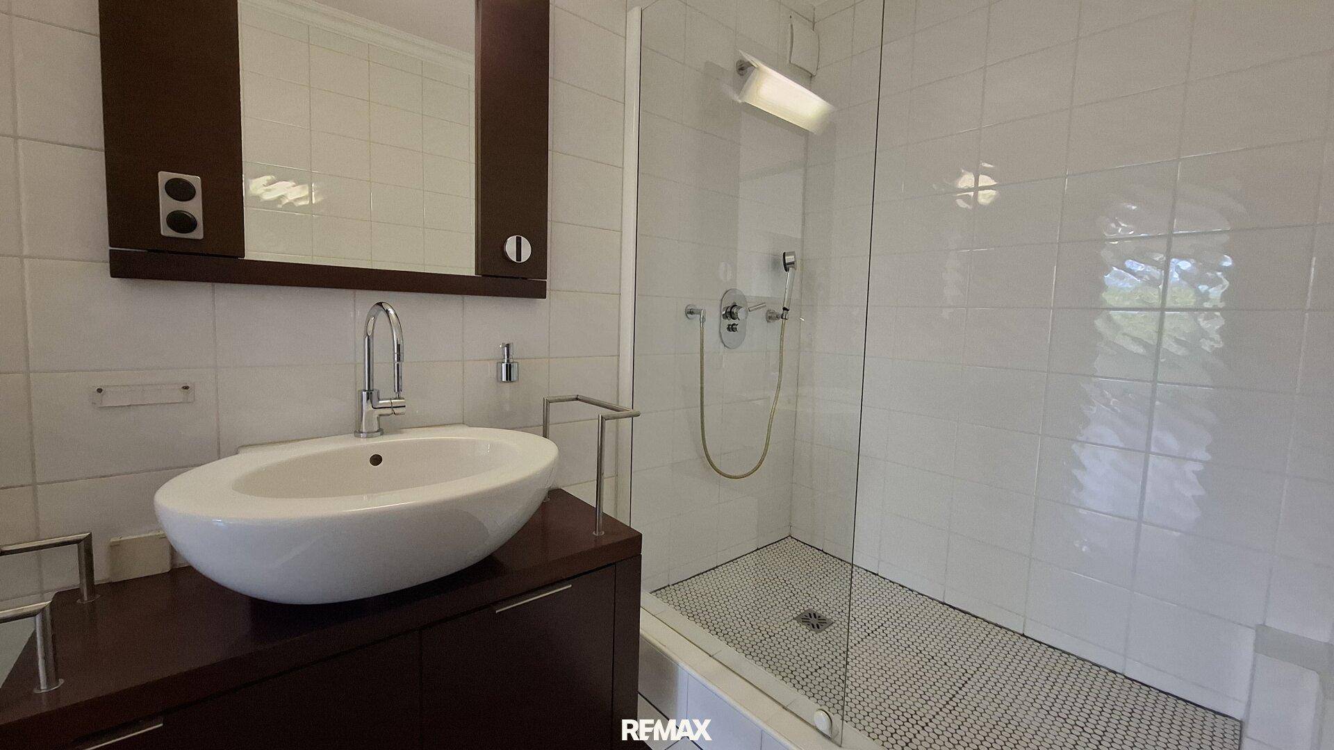 Modernes Badezimmer mit weißen Fliesen, Einzelwaschbecken und einer begehbaren Dusche mit Glaswand.