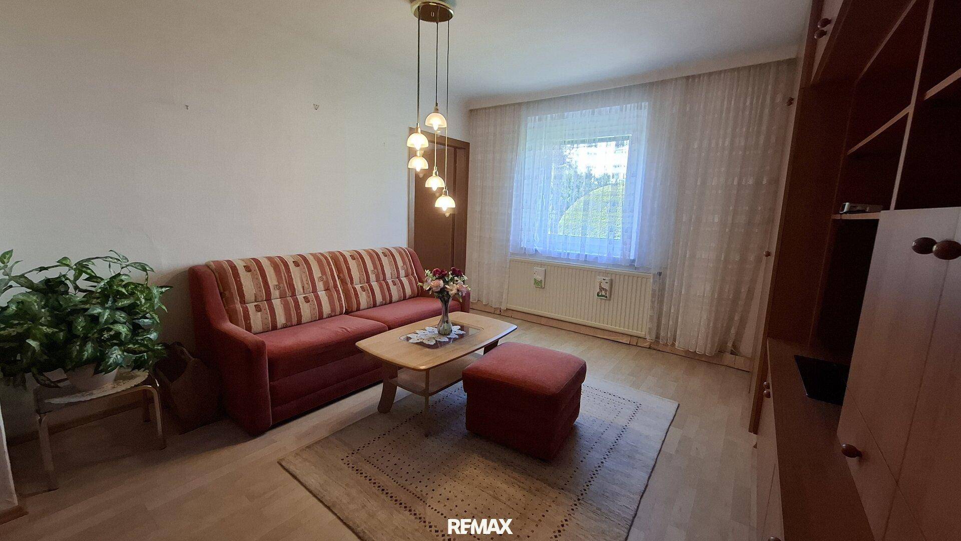 Helles Wohnzimmer mit rotem Sofa, Couchtisch und Teppich, bietet eine gemütliche Atmosphäre.