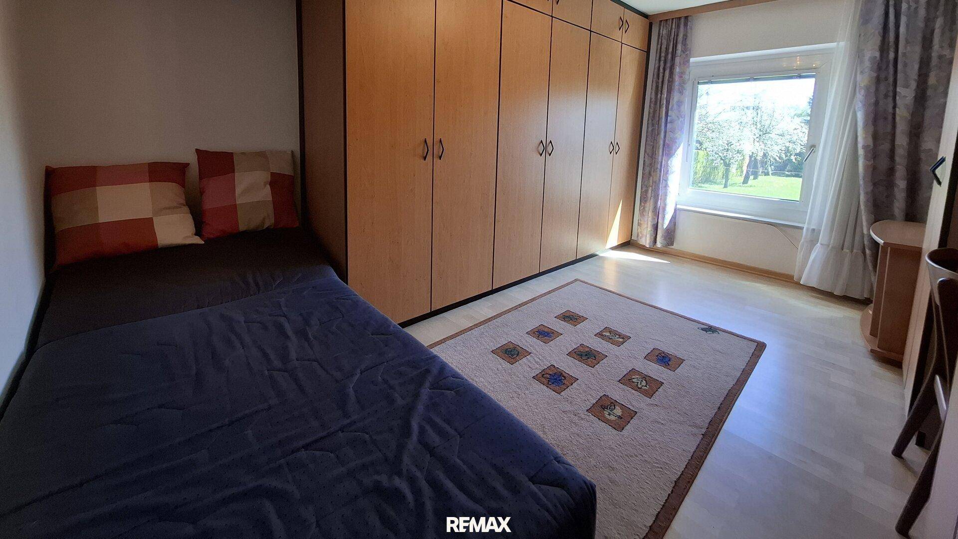 Helles Schlafzimmer mit Einzelbett, Holzschränken und Blick ins Grüne, ideal als Gästezimmer.