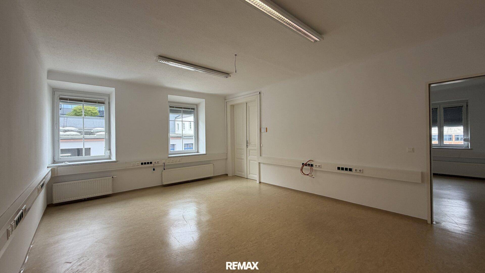 Heller Büroraum mit Linoleumboden und mehreren Fenstern, die viel Tageslicht hereinlassen.
