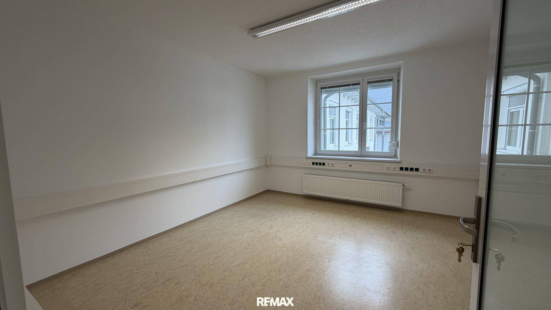 Heller Büroraum mit Linoleumboden und großem Fenster, gut beleuchtet und funktional eingerichtet.