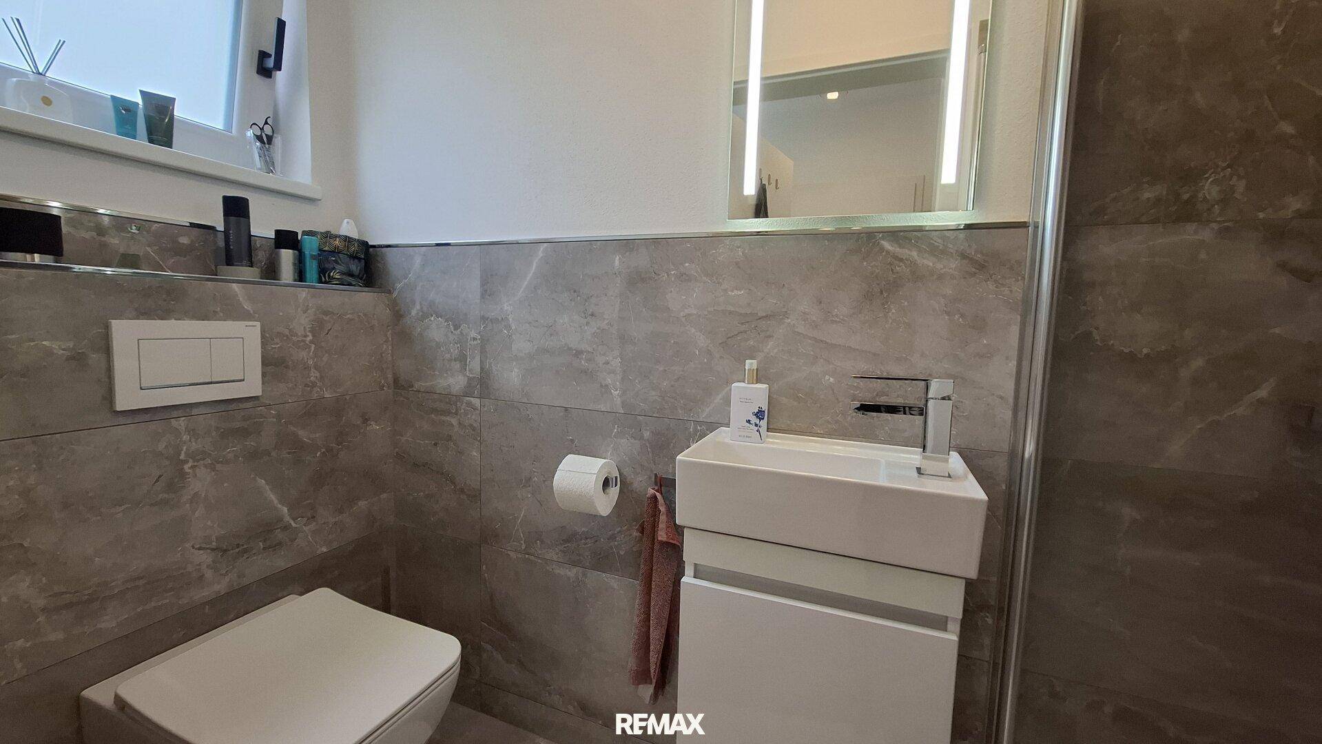 Modernes Badezimmer mit grauen Marmorfliesen, wandhängendem WC und Dusche.