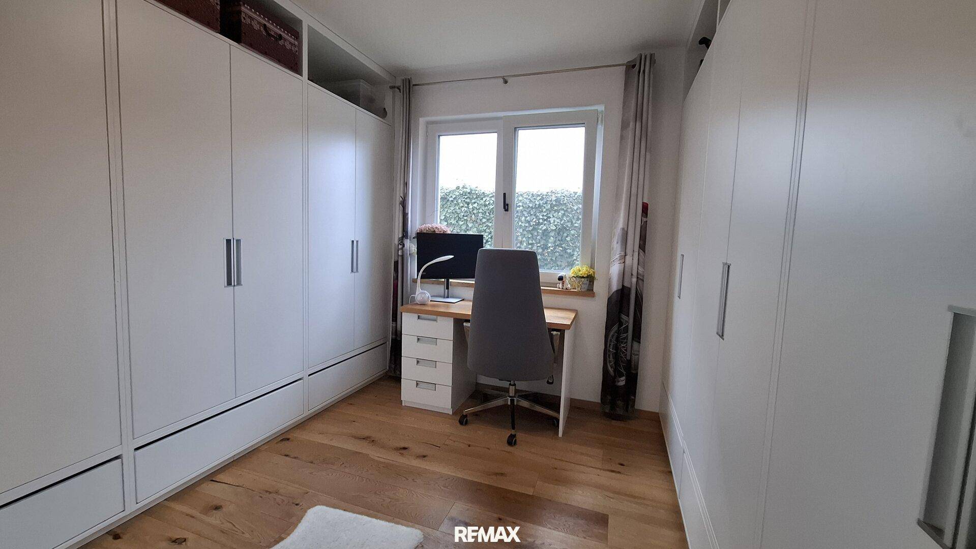 Helles Arbeitszimmer mit Einbauschränken, Schreibtisch am Fenster und Holzboden.