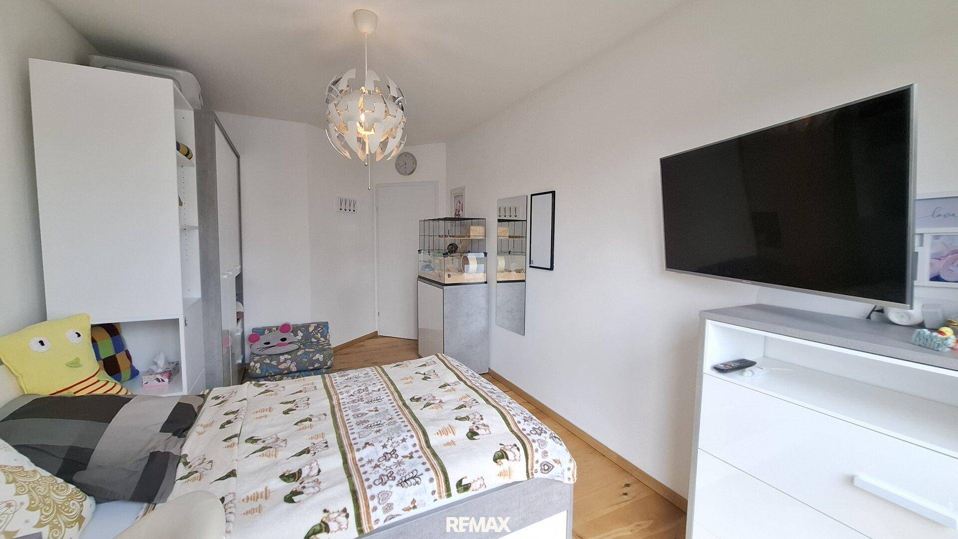 Gemütliches Schlafzimmer mit Bett, weißem Kleiderschrank und Wandfernseher.
