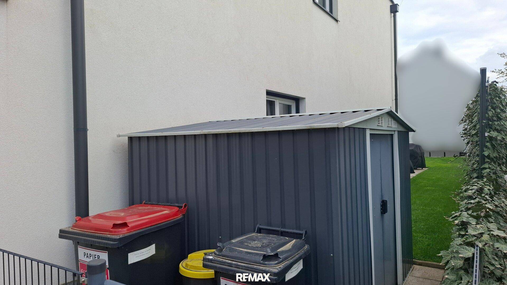 Kleiner Geräteschuppen im Gartenbereich neben dem Haus und Mülltonnen.