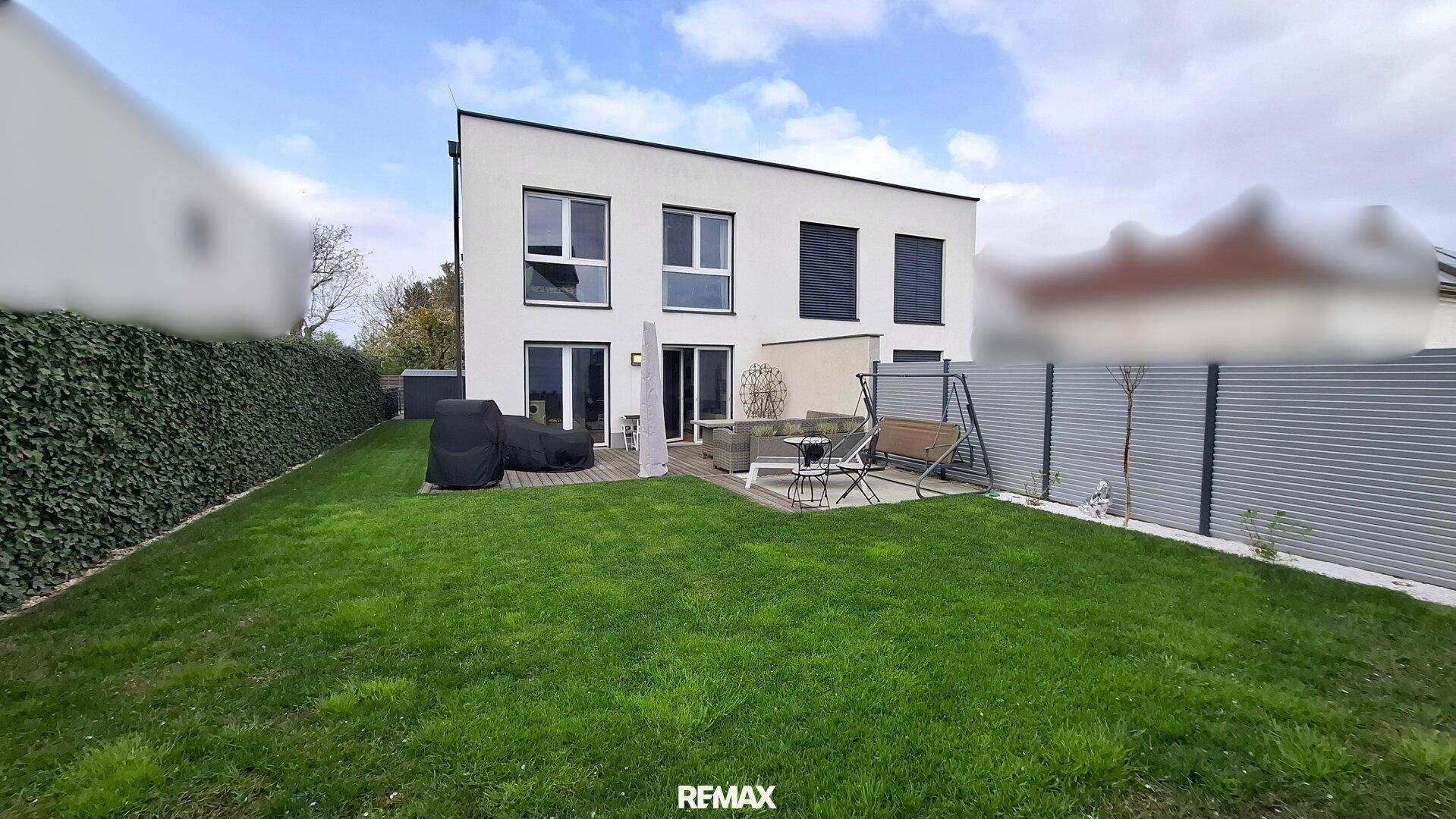 Hinterhof mit Rasenfläche, Holzterrasse und Gartenmöbeln, umgeben von einer Hecke.