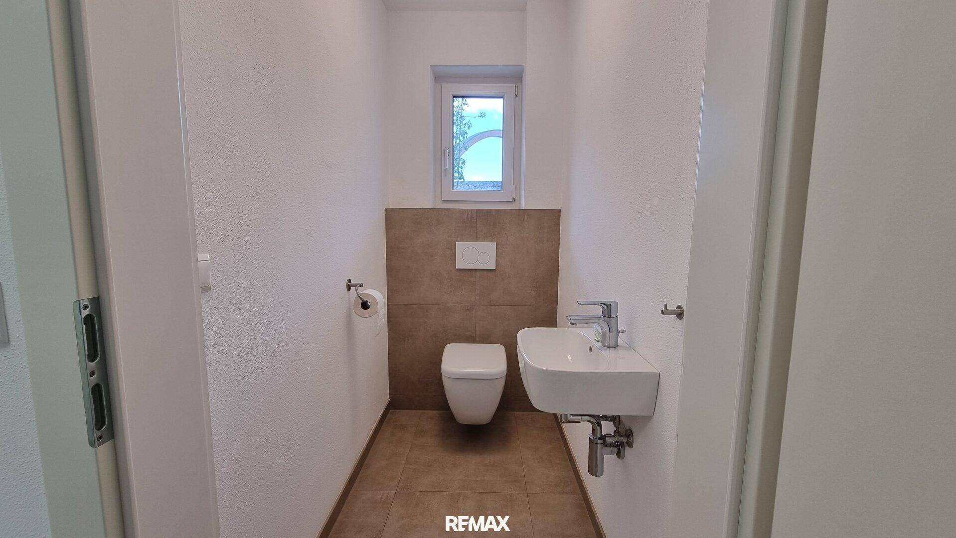 Modernes Gäste-WC mit wandhängender Toilette, kleinem Waschbecken und Fenster für Tageslicht.