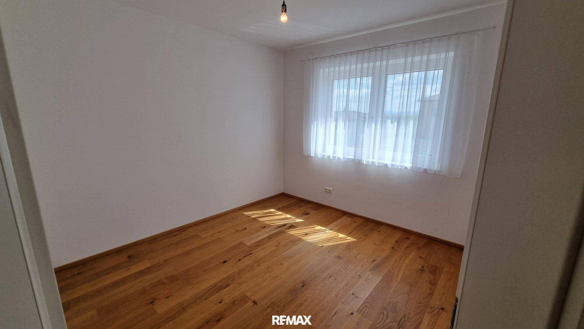 Helles Schlafzimmer mit Holzboden und großem Fenster, das viel Tageslicht hereinlässt.