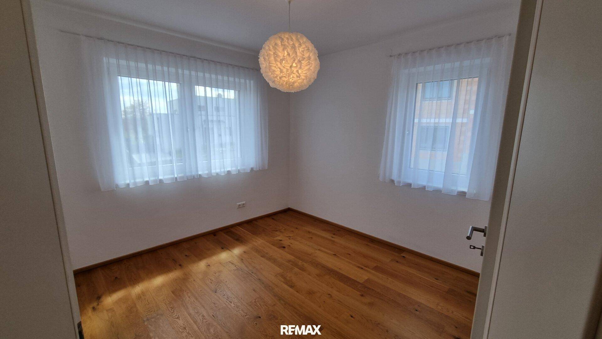 Schlafzimmer mit zwei Fenstern und Holzboden, bietet eine helle und freundliche Atmosphäre.