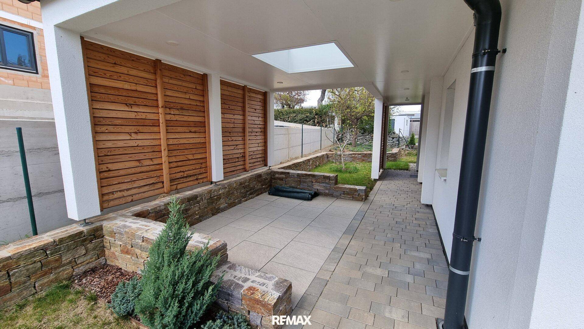 Überdachte Terrasse mit Steinmauern, Holzelementen und einem Oberlicht, ideal für Entspannung im Freien.