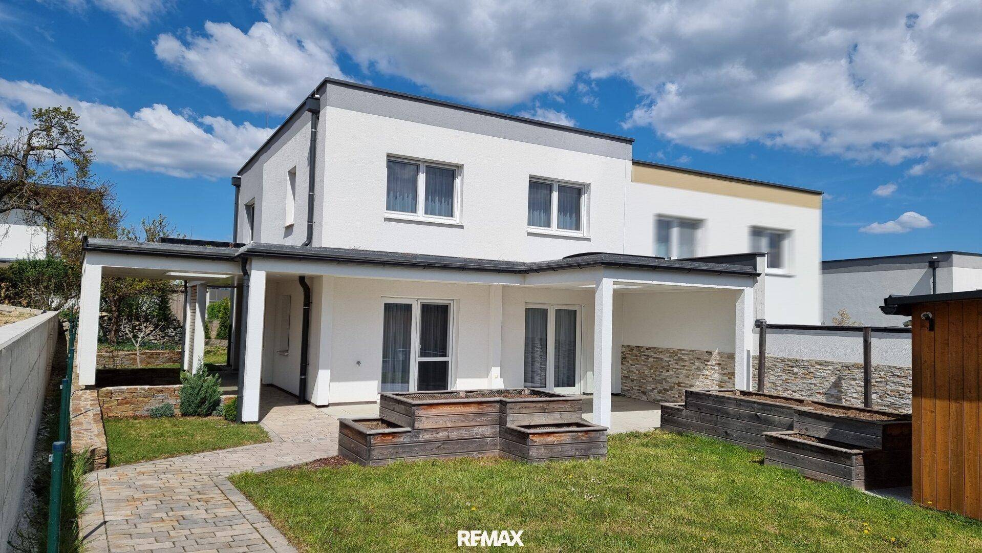 Ansicht des modernen Hauses von außen mit Rasenfläche und dekorativen Hochbeeten.