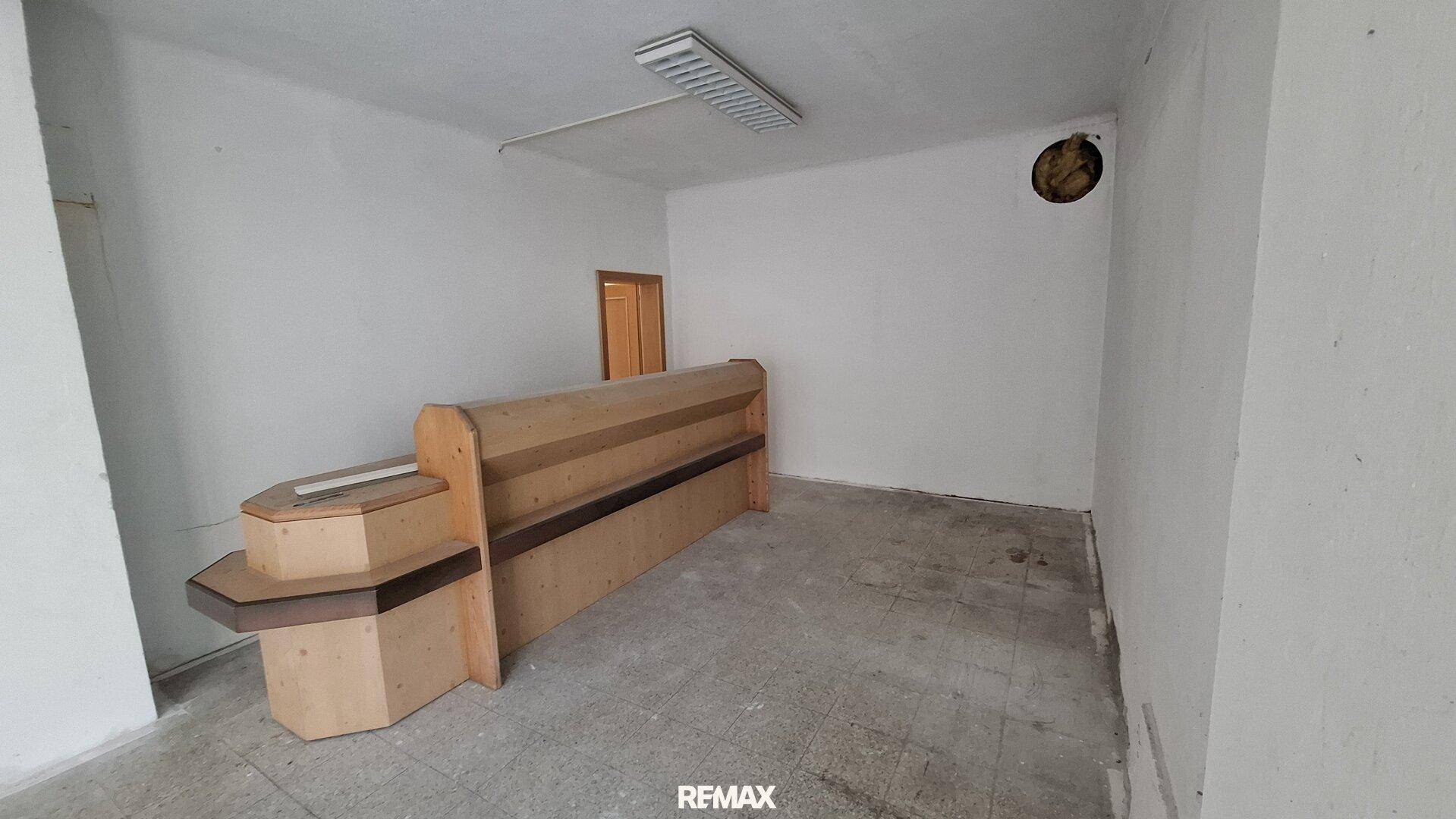 Leerer Raum mit einem Holztresen, Fliesenboden und einer Tür im Hintergrund.