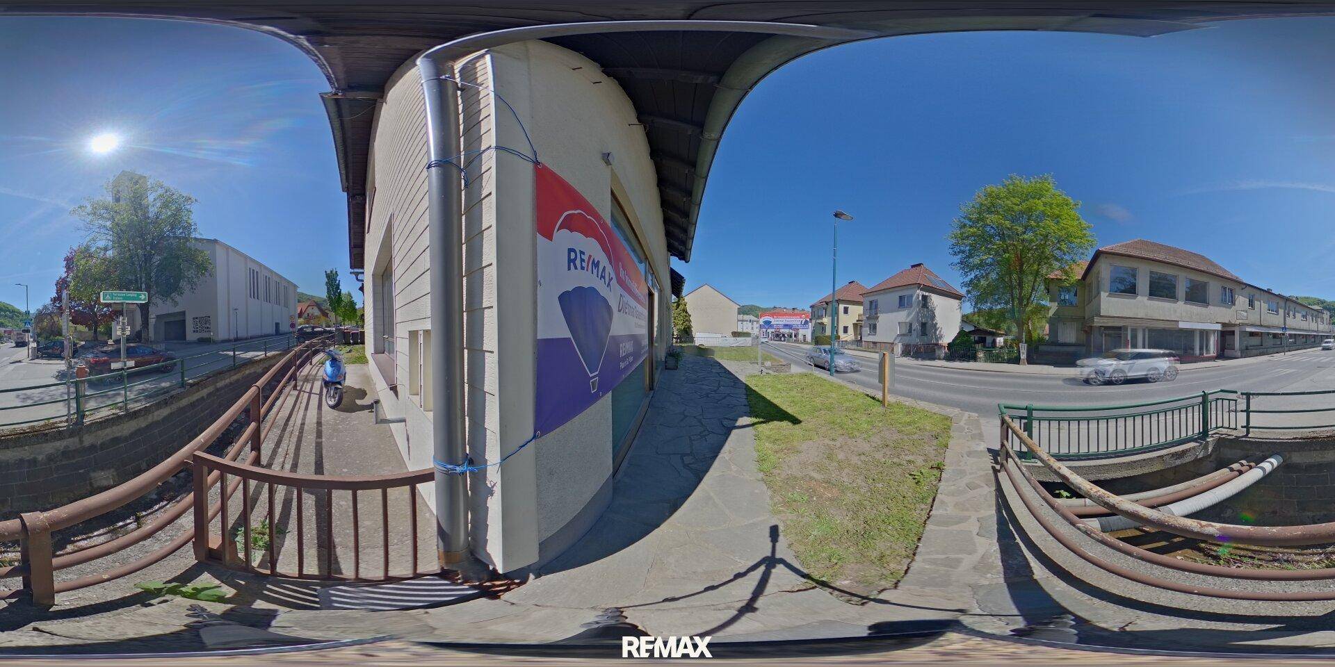 Panoramablick auf die Seitenansicht des Gebäudes mit einem kleinen Bach und der Straße.