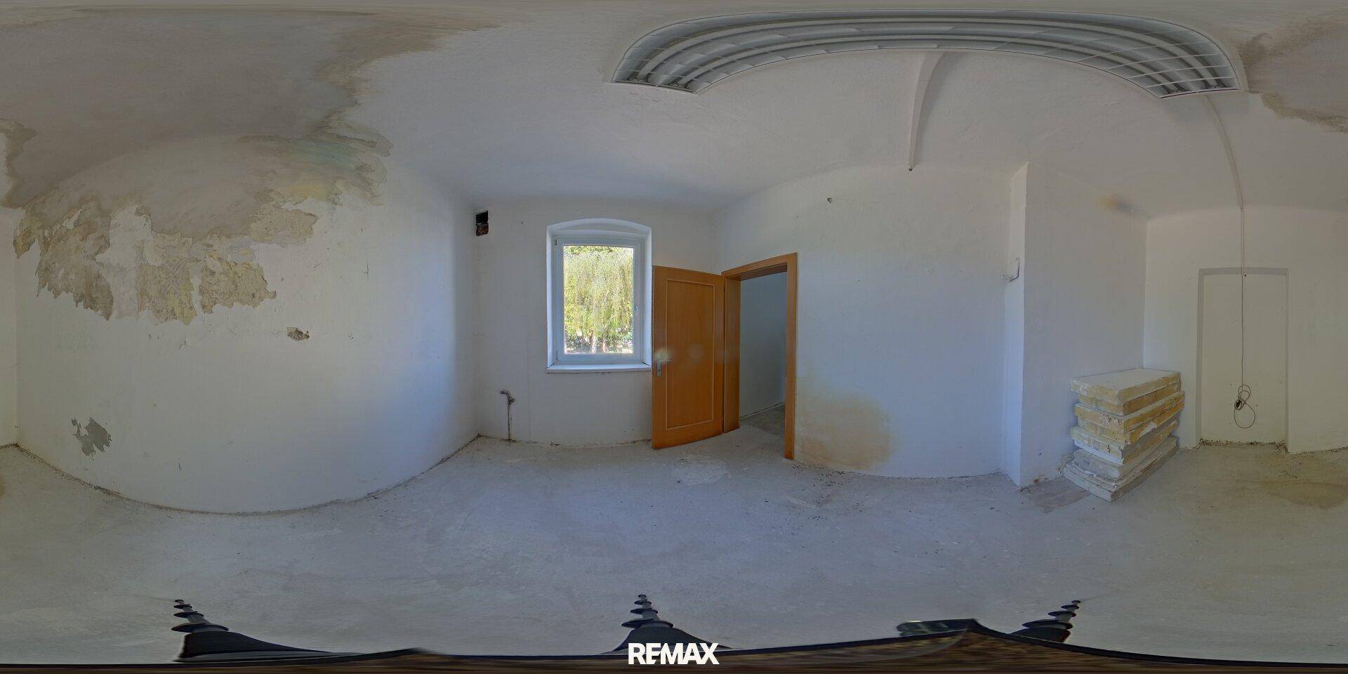 Leerer Raum mit einem Fenster und offener Holztür, bereit für die Renovierung und mit Blick ins Grüne.