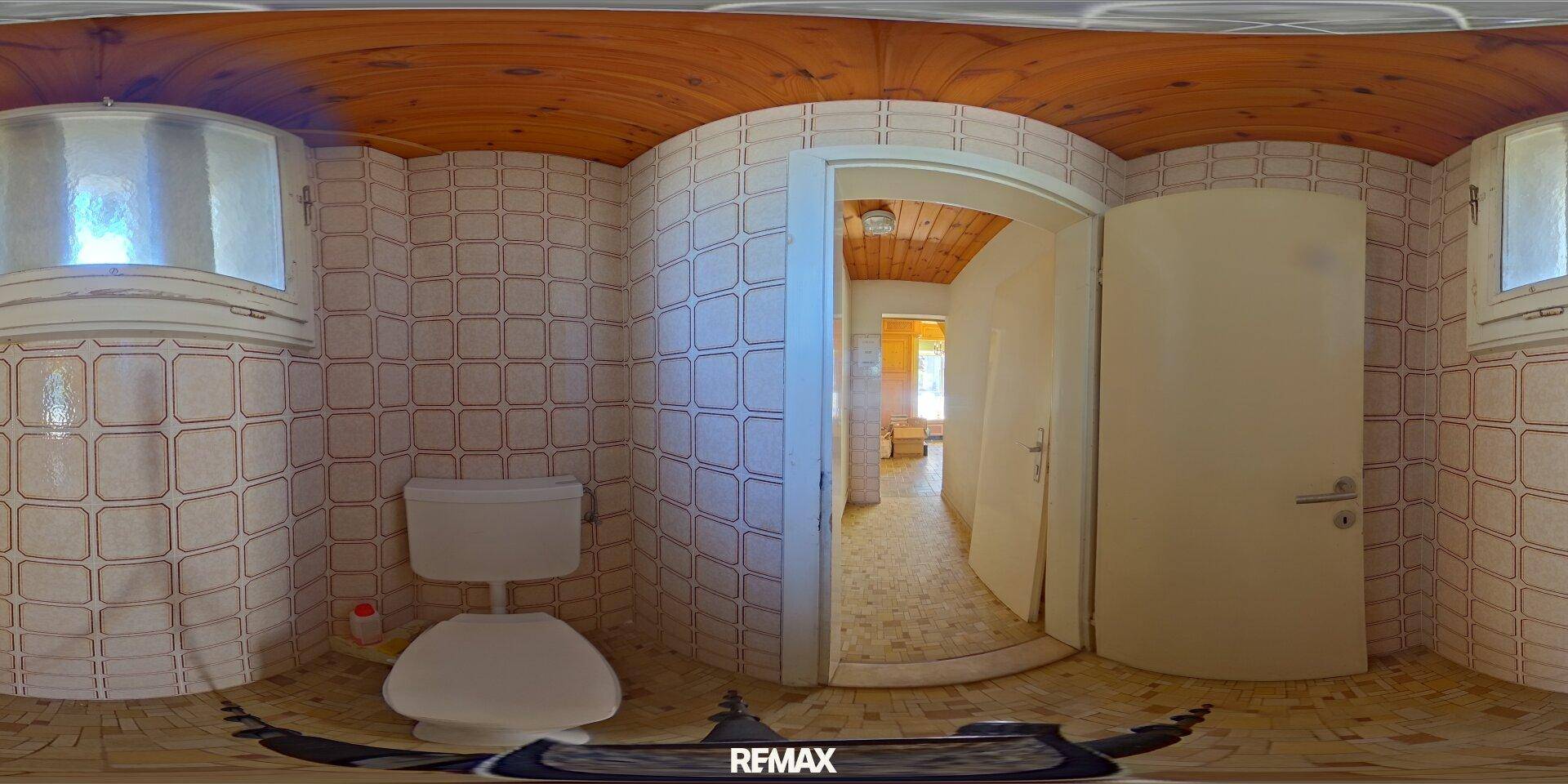Panoramablick auf eine Toilette mit Fliesenwänden, Holzdecke und zwei kleinen Fenstern.