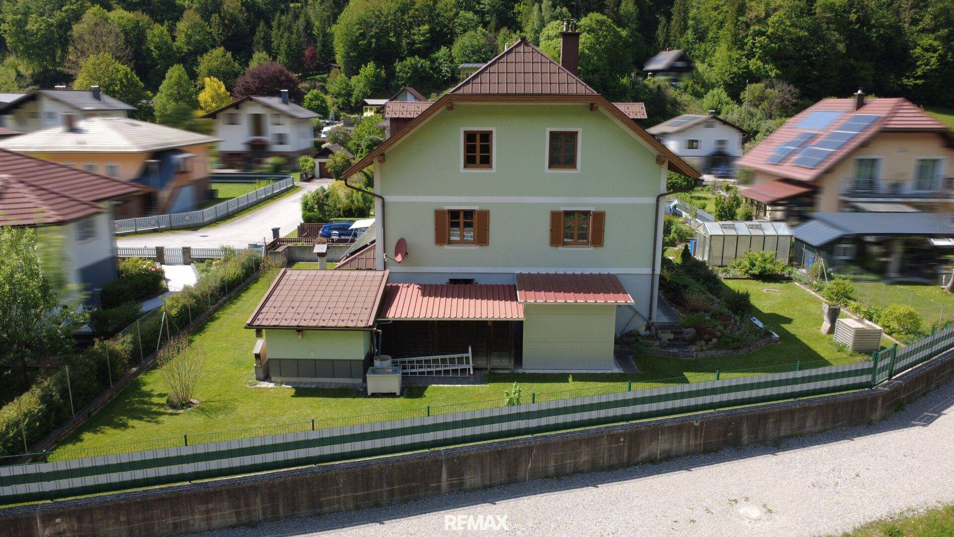 Ansicht des Hauses mit hellgrüner Fassade, braunem Dach und umzäuntem Gartenbereich.
