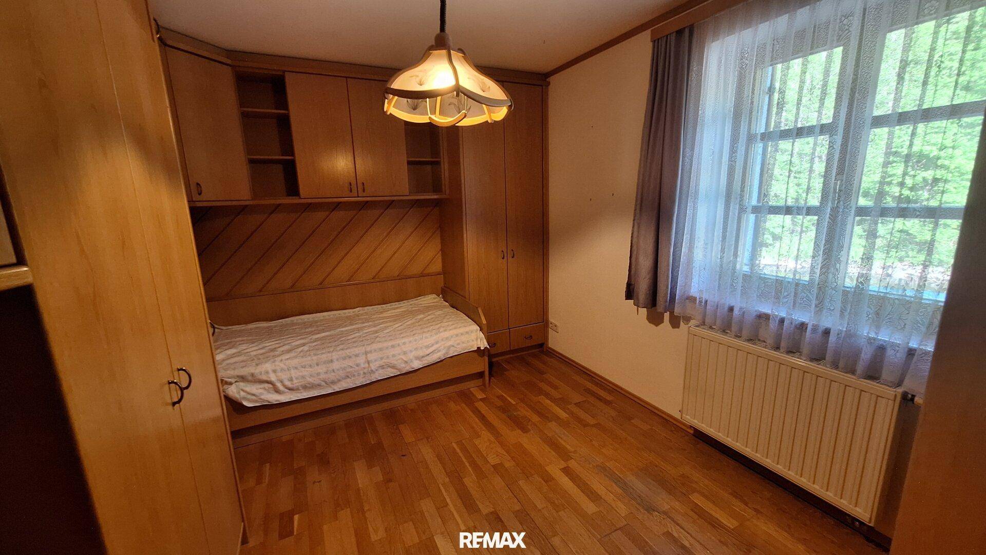 Gemütliches Schlafzimmer mit Holzboden, Einbauschränken und Fenster mit Blick ins Grüne.