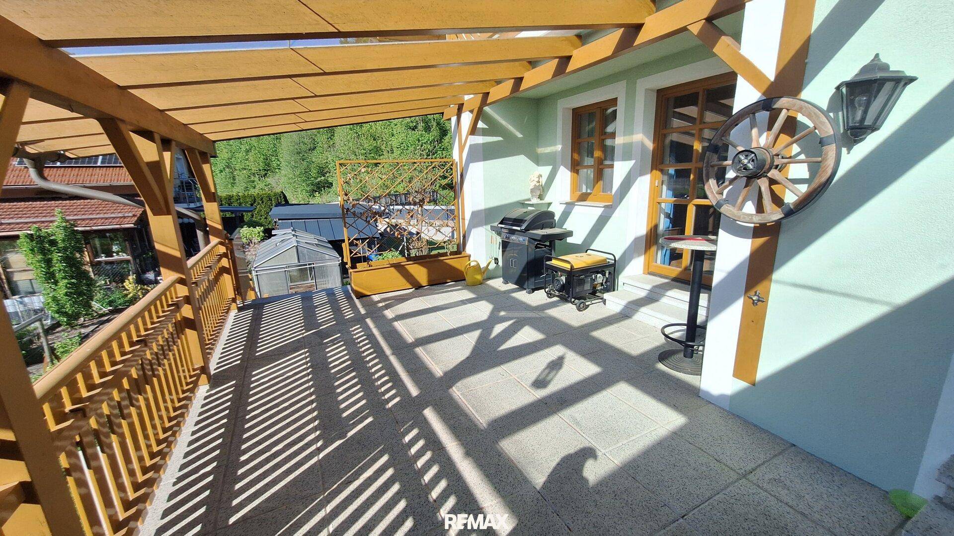 Überdachte Terrasse mit Fliesenboden, Grillbereich und Blick auf den Garten.