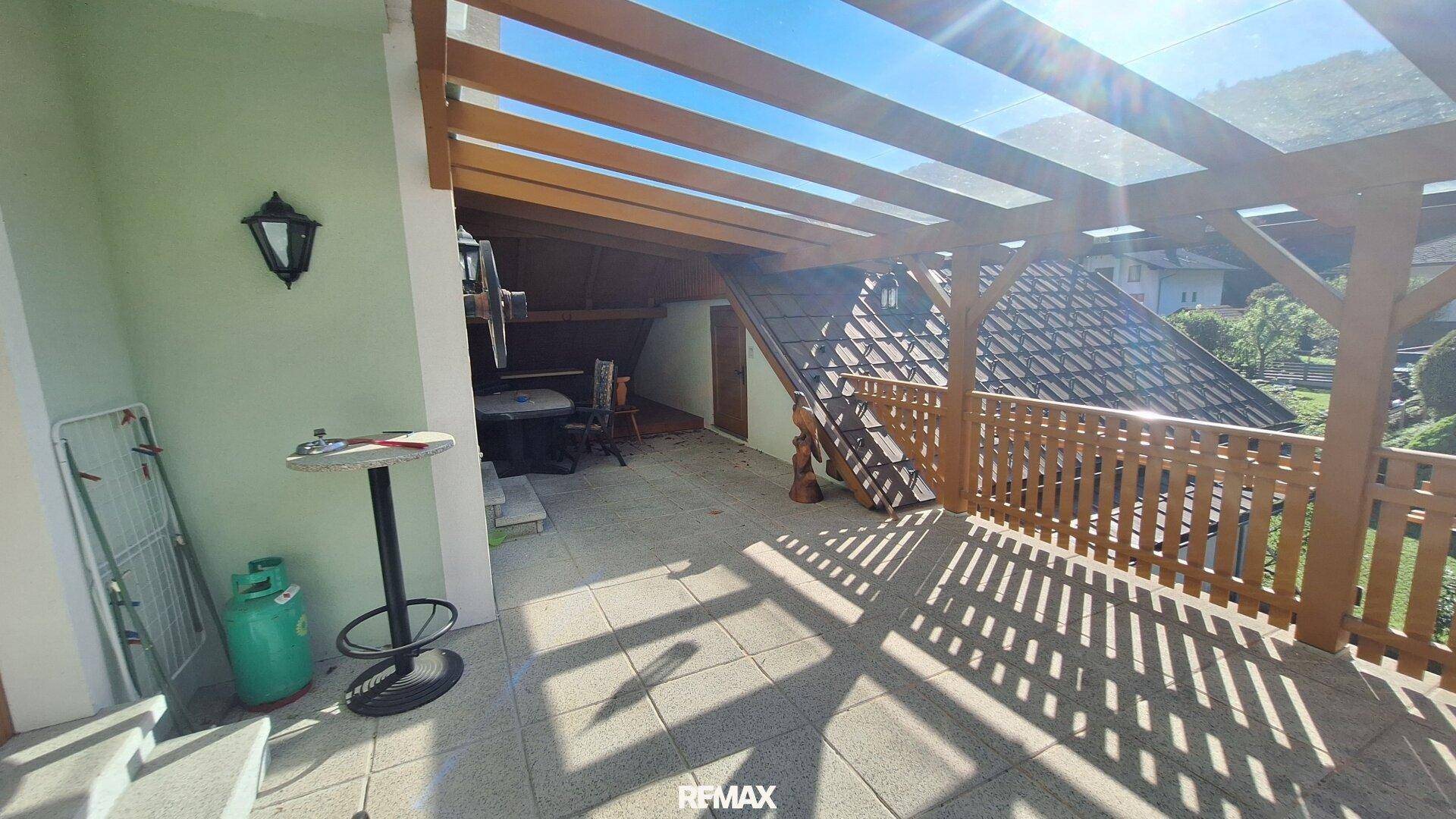 Geräumige, überdachte Terrasse mit Fliesenboden und Holzbalken, ideal zum Entspannen im Freien.