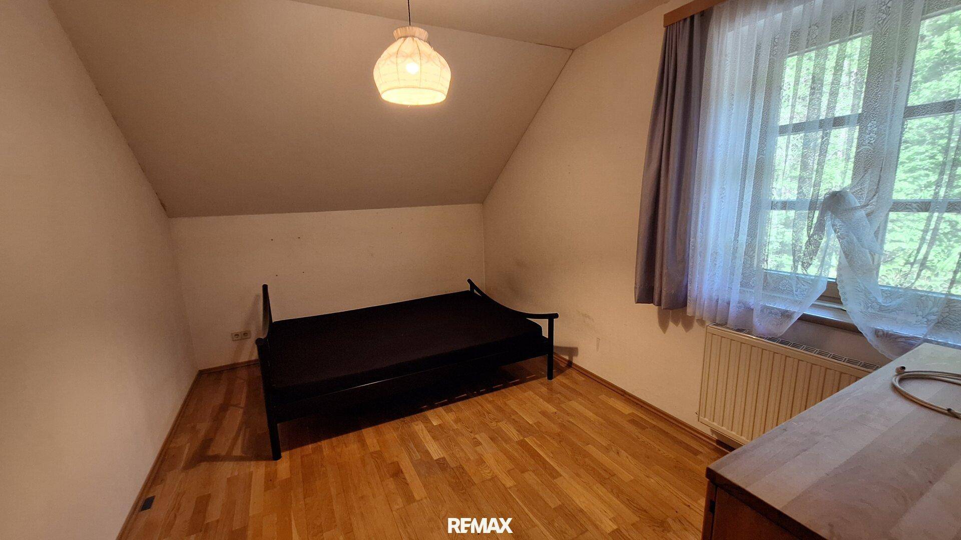 Helles Schlafzimmer im Dachgeschoss mit Holzboden, Einzelbett und Dachschräge.